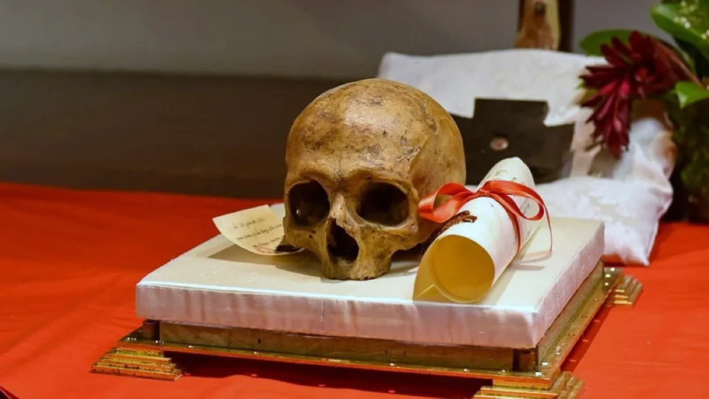 A skull and scroll lie on a white cloth on a gold pedestal