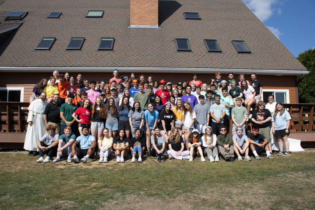 A groups poses in front large house with chimney and skylights.